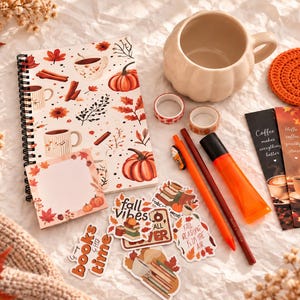 May include: A spiral-bound notebook with an autumnal pattern of pumpkins, leaves, and coffee mugs, a pumpkin-shaped ceramic mug, a crochet pumpkin coaster, two bookmarks with coffee text, stickers, two pens, a highlighter, and two rolls of washi tape.