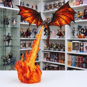 May include: A detailed dragon figurine with expansive, dark-veined orange and red wings, suspended in mid-air while breathing a long, translucent stream of yellow and orange fire that connects to a large, sculpted base of swirling flames.