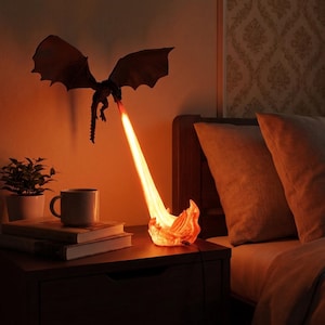 Op de afbeelding: Een donkerbruin drakenfiguur gemonteerd aan de muur, die een heldere oranje lichtstraal uitstraalt die naar beneden reikt naar een gebeeldhouwde basis die op vlammen lijkt. Het licht verlicht de omgeving met een warme, vurige oranje gloed.