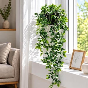 May include: A trailing artificial plant with vibrant green leaves cascading from a black pot. The plant features multiple stems with variegated foliage in shades of light and dark green, creating a lush, full appearance as it hangs downward.