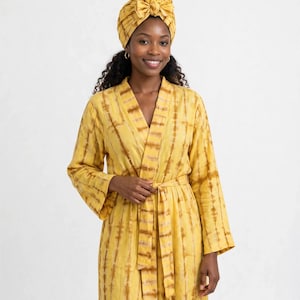 May include: A yellow robe with a brown tie-dye vertical stripe pattern, featuring long sleeves, a wrap-front design with a matching fabric belt, and a coordinating yellow tie-dye head wrap with a decorative bow detail on the front.