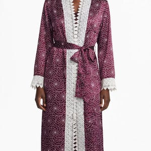Peut inclure: Une robe de chambre bordeaux à manches longues avec un motif tourbillonnant blanc, une bordure en dentelle blanche le long de l'ouverture avant et des poignets, et une ceinture assortie. L'ensemble comprend un bonnet bordeaux assorti.