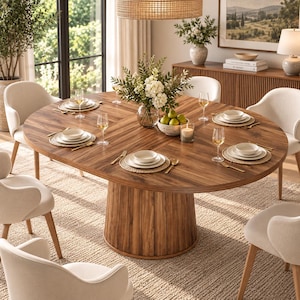 May include: A round wooden dining table with a central pedestal base, surrounded by six cream-colored upholstered chairs. The table is set with white ceramic plates, bowls, wine glasses, gold cutlery, and woven placemats, featuring a floral centerpiece.