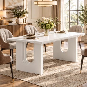 May include: A rectangular white dining table featuring two U-shaped pedestal bases with grooved detailing. The table is set with clear glassware, white plates, and gold-toned cutlery, surrounded by four upholstered chairs with beige and brown fabric.