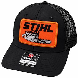 May include: A black trucker hat featuring a mesh back and a rectangular orange patch on the front. The patch displays the black text STIHL above an embroidered graphic of a chainsaw with the word STIHL on the bar. A black sticker is on the brim.