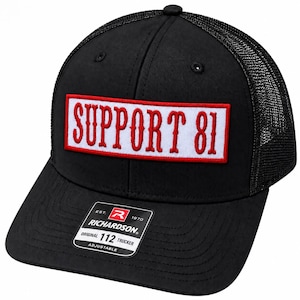 May include: A black trucker hat with a mesh back and a solid front panel. A rectangular white patch with a red border is centered on the front, featuring the red text SUPPORT 81. A black and white sticker on the brim reads RICHARDSON 112 TRUCKER.