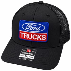 May include: A black trucker hat featuring a rectangular patch with the blue Ford logo above the white text TRUCKS on a red background. The front panel is solid black, while the back panels are made of black mesh. A sticker on the brim reads RICHARDSON 112 TRUCKER.