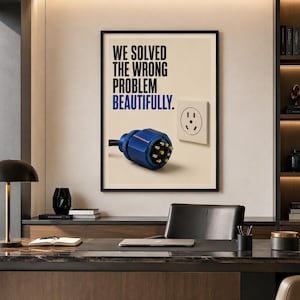 Könnte beinhalten: Ein gerahmter Kunstdruck mit dem Text WE SOLVED THE WRONG PROBLEM BEAUTIFULLY in Schwarz und Blau. Die Grafik zeigt einen blauen industriellen Netzstecker mit goldenen Stiften neben einer Standard-Wandsteckdose auf cremefarbenem Grund.