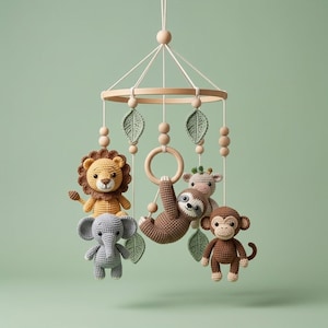 May include: A nursery mobile featuring a circular wooden frame with hanging crochet figures of a lion, elephant, sloth, monkey, and giraffe. The mobile includes green crocheted leaves and wooden beads suspended by white strings from a central point.