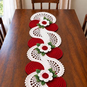 May include: A long, decorative table runner featuring a repeating pattern of white crocheted lace sections with openwork designs, alternating with solid red circular crocheted mats, accented by three white flowers with red centers and green leaves.