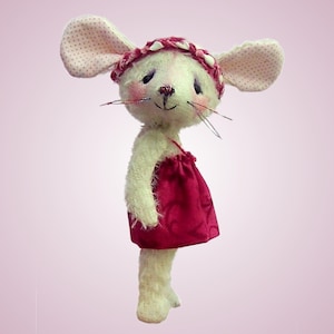 May include: A handcrafted fabric mouse doll with cream-coloured fur, large ears featuring a pink polka dot pattern, and rosy cheeks. The mouse wears a dark red dress with a subtle swirling pattern and a matching braided headband with small white accents.