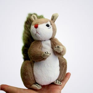 May include: A plush squirrel toy featuring soft brown and white fur, a bushy tail, small pointed ears, and a distinct red nose. The stuffed animal is depicted in a seated position with its front paws raised, showcasing a textured fabric finish.