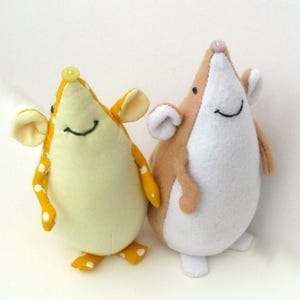 May include: Two plush mouse toys standing side by side. The left mouse is yellow with white polka dots and a yellow button nose. The right mouse is tan and white with a small pink button nose. Both have embroidered smiles and large ears.