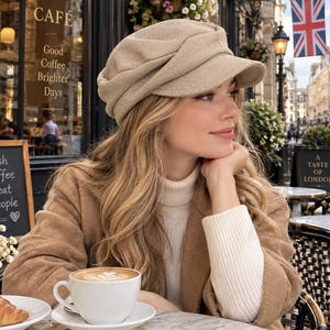 May include: A beige newsboy cap with a structured brim and a soft, rounded crown. The hat features a textured fabric finish and a classic multi-paneled construction, providing a fitted look that sits comfortably on the head with a short, stiff visor.