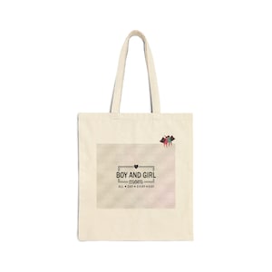 May include: A beige canvas tote bag featuring a rectangular graphic with the text BOY AND GIRL mom ALL DAY EVERY DAY and a small heart icon. Above the text, a small illustration depicts two figures in red and blue clothing standing together.