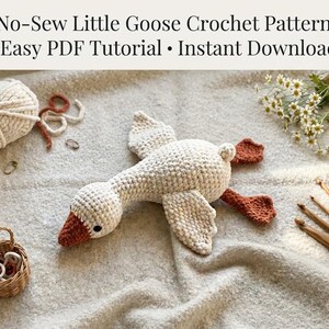 Könnte beinhalten: Eine Häkelanleitung mit dem Titel No-Sew Little Goose Crochet Pattern Easy PDF Tutorial Instant Download, die eine cremefarbene gehäkelte Gans mit orangefarbenem Schnabel und Füßen zeigt, begleitet von einem Garnknäuel, einem kleinen Korb und Holzhäkelnadeln.