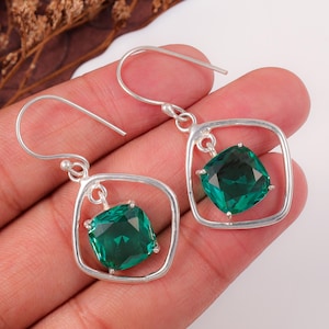 Peut inclure: Une paire de boucles d'oreilles pendantes en argent avec un design de cadre carré. Chaque boucle d'oreille contient une pierre précieuse vert émeraude taillée en coussin et facettée, suspendue au centre par des crochets en argent.