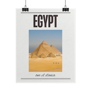 May include: A white poster featuring the word EGYPT in large black capital letters at the top and the text om el donia in black script at the bottom. The center displays a photograph of the Giza pyramids in a desert landscape with camels.