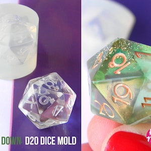 Op de afbeelding: Een transparante plastic mal voor het maken van een 20-zijdige dobbelsteen. De mal is cilindrisch en heeft een 20-zijdige dobbelsteen erin. De mal ligt naast een groene en transparante 20-zijdige dobbelsteen met gouden glitter en koperen cijfers. De tekst "COUNT DOWN D20 DICE MOLD" staat onderaan de afbeelding.