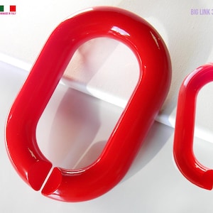 Puede incluir: Dos moldes rojos brillantes con forma de eslabón de cadena ovalado. El molde más grande mide aproximadamente 20 cm de largo, mientras que el más pequeño mide unos 10 cm. Los moldes están hechos en Italia y están diseñados para manualidades. El texto "BIG LINK 3D CHAIN CLEAR MOLD" es visible.