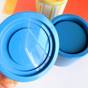 May include: A blue silicone mould set for making a jar with a lid. The mould is made in Italy and is handmade. The mould is shown in two parts, the jar and the lid. The lid mould has a raised rim around the edge. The jar mould is a cylinder with a flat bottom. The mould is made of a flexible silicone material.