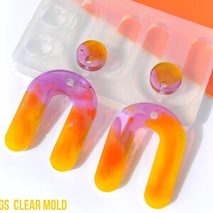 May include: Two pairs of colorful resin earrings in a clear mold. The earrings are shaped like an upside down U and are a mix of yellow, orange, and purple.