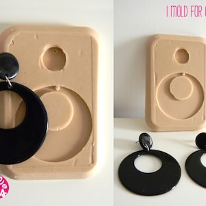 May include: A silicone mold for making earrings. The mold is beige and has two circular cavities. Two black earrings are shown next to the mold.