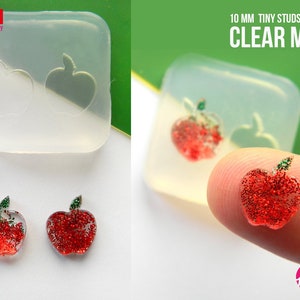 May include: Clear silicone mold for making 10 mm apple-shaped stud earrings. The mold is shown with two finished earrings, each with red glitter and a green leaf.