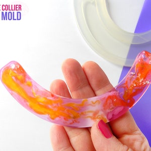 Puede incluir: Un molde de silicona transparente para hacer un colgante o collar de resina en forma de gran sonrisa. El molde se muestra con una pieza de resina terminada en colores rosa, naranja y amarillo. El texto "BIG SMILE COLLIER CLEAR MOLD" es visible en la imagen.
