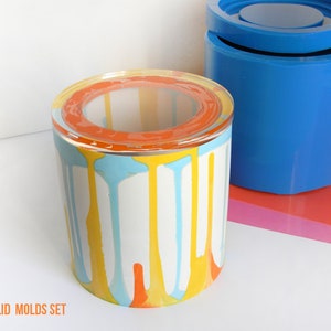 May include: A set of two silicone moulds for making a jar with a lid. The moulds are blue and the jar is shown in a colourful drip pattern with orange, yellow, and blue paint.