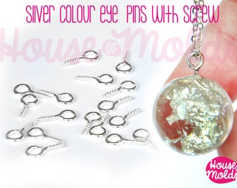 May include: Silver eye pins with screw backs. The pins are scattered on a white surface. A silver chain with a clear glass pendant is in the background.