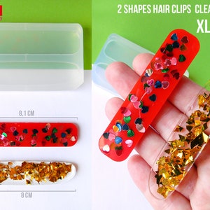 Peut inclure: Moule en silicone transparent pour la fabrication de deux formes de pinces à cheveux. Le moule mesure 8,1 cm de long et 8 cm de large. Le moule est présenté avec deux pinces à cheveux finies, l'une avec de la résine rouge et des cœurs colorés, et l'autre avec de la résine transparente et des paillettes dorées.