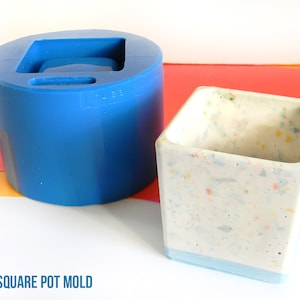 Könnte beinhalten: Eine blaue Silikonform zum Herstellen eines quadratischen Pflanzgefäßes. Die Form befindet sich neben einem fertigen Pflanzgefäß aus weißem Beton mit bunten Flecken. Das Pflanzgefäß hat einen blauen Streifen um den oberen Rand. Der Text "SMALL SQUARE POT MOLD" befindet sich am unteren Rand des Bildes. Der Text "House Molds" befindet sich in einem roten Kreis unten rechts im Bild.