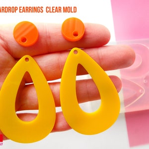 May include: A clear silicone mold for making teardrop-shaped earrings. The mold is shown with two yellow teardrop earrings and two orange round earrings.