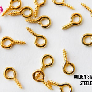May include: A close-up of a variety of gold-coloured metal eyelets with screw backs. The eyelets are arranged on a white surface. The text "GOLDEN STAINLESS STEEL EYE PINS" is visible in the lower right corner of the image.