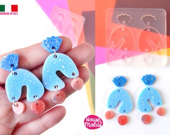 Könnte beinhalten: Ein Paar blaue und weiße, gesprenkelte Harzohrringe mit einem kleinen rosa und roten Akzent. Die Ohrringe werden mit einer Silikonform hergestellt, die ebenfalls abgebildet ist. Die Form ist klar und hat zwei große Bogenformen, zwei kleine Kreise und zwei kleine Tropfenformen. Der Text "Handmade in Italy" und "House of Molds" ist auf dem Bild zu sehen.