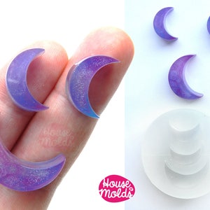 Puede incluir: Un juego de cuatro moldes de silicona en forma de media luna de color púrpura iridiscente. Los moldes se muestran con las piezas de resina terminadas. Los moldes están hechos por House Molds.