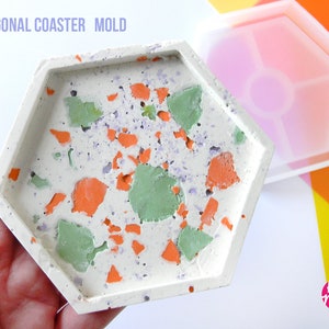 May include: A white hexagonal coaster mould with a finished coaster inside. The coaster has a terrazzo design with orange, green, and purple flecks. The mould is made of silicone and is flexible. The text "House Molds" is visible in the lower right corner of the image.