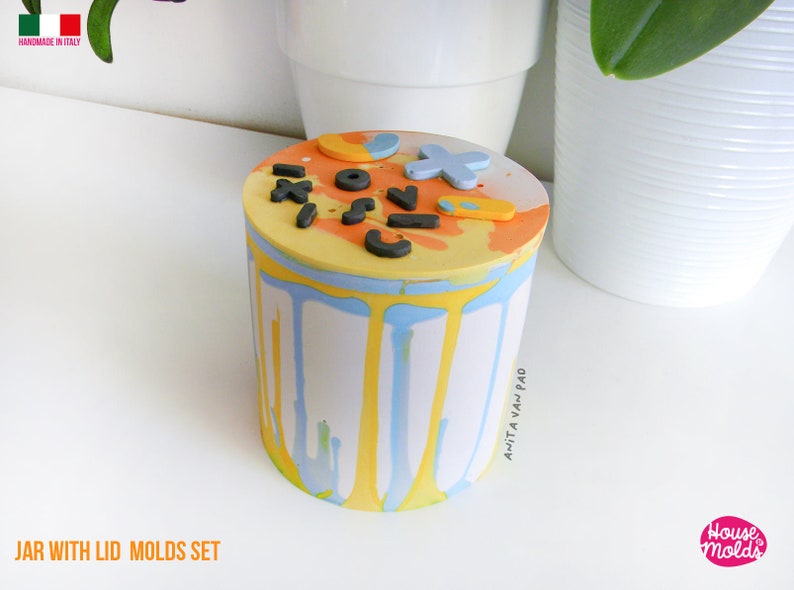 May include: A colourful, abstractly painted jar with lid mould set. The jar is decorated with yellow, blue and orange paint and has a variety of shapes and letters on the lid. The jar is labelled "Anita Van Pad" and "Handmade in Italy".