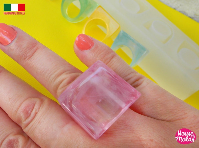 May include: A pink square ring made of resin. The ring is on a finger and the background is yellow.
