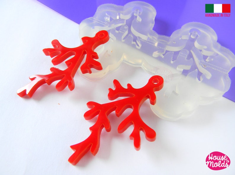 May include: Two red resin coral branch charms with a hole for hanging. The charms are next to a clear silicone mold of the same design. The mold is labeled "Handmade in Italy".
