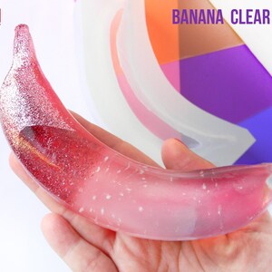 Könnte beinhalten: Eine transparente Silikonform in Form einer Banane. Die Form wird mit einem rosa und weißen Harzgussteil gezeigt. Die Form ist handgefertigt in Italien. Der Text "BANANA CLEAR MOLD" ist im Bild sichtbar.