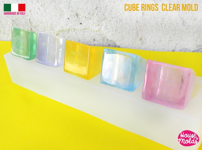 May include: Five clear cube-shaped rings in different colors: green, purple, yellow, blue, and pink. The rings are displayed on a white silicone mold. The text "CUBE RINGS CLEAR MOLD" is visible at the top of the image.