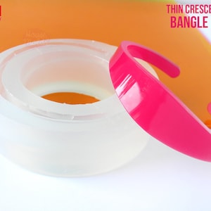 May include: A clear silicone mold for making thin crescent cuff bracelets. The mold is shown with a pink resin bracelet that has been cast in the mold. The mold is handmade in Italy.