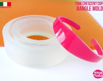 May include: A clear silicone mold for making thin crescent cuff bracelets. The mold is shown with a pink resin bracelet that has been cast in the mold. The mold is handmade in Italy.