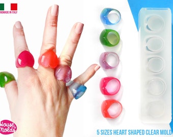 May include: Five clear silicone molds for making heart-shaped rings. The molds are arranged in a row, with each mold containing a different size heart. The molds are made in Italy.