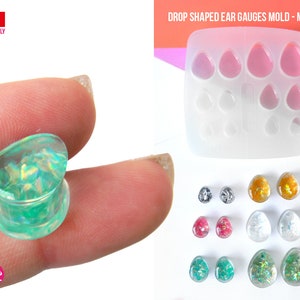 May include: A clear silicone mold for making teardrop shaped ear gauges. The mold has six cavities in a 2x3 grid. The mold is shown with finished ear gauges in various colors and glitter.
