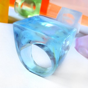 May include: A light blue, square-shaped resin ring with a clear, translucent finish. The ring is handmade in Italy.