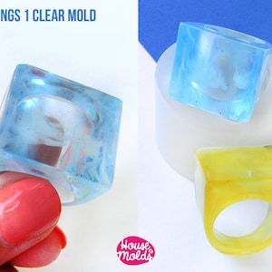 Può includere: Due anelli in resina trasparente a forma di cubo. Un anello è azzurro chiaro e l'altro è giallo. Gli anelli sono realizzati con uno stampo in silicone. Lo stampo è bianco e presenta il testo "House Molds".