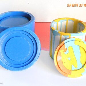 May include: Two silicone moulds for making a jar with a lid. The moulds are blue and show the finished product in a colourful abstract design. The text "JAR WITH LID MOLDS SET" is at the top of the image. The text "House Molds" is at the bottom of the image.